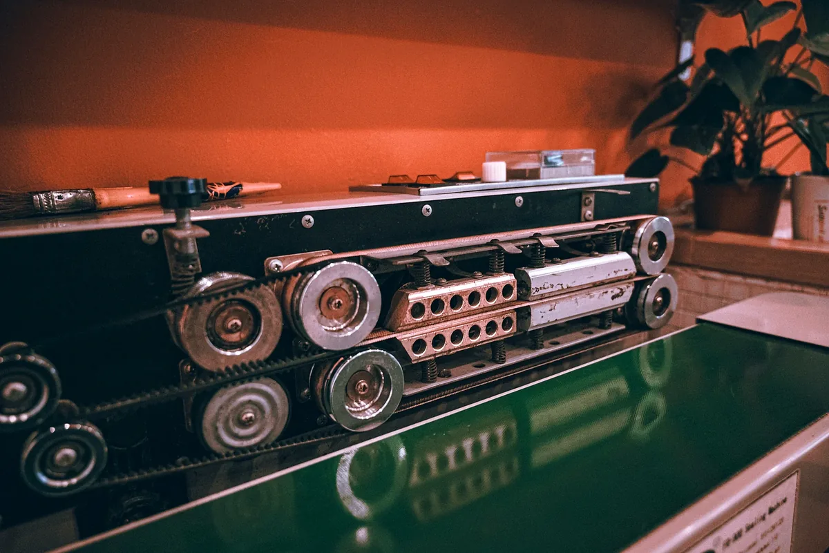 Small green conveyor belt beside exposed wheels and metal machine parts.