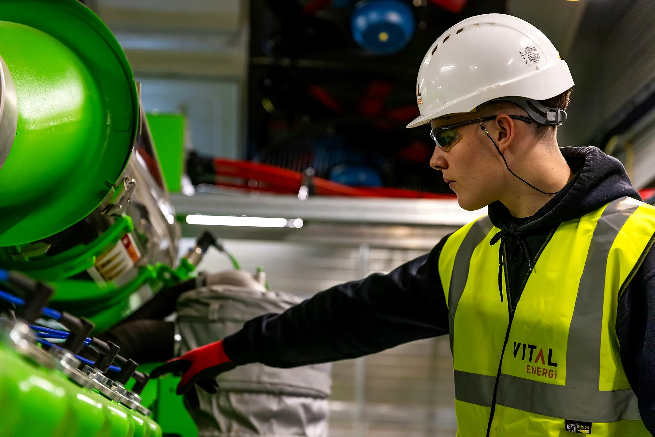 Worker in a hard hat and high-visibility vest beside green industrial equipment.