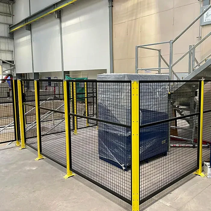 Black mesh fencing with yellow posts around wrapped goods in a warehouse.