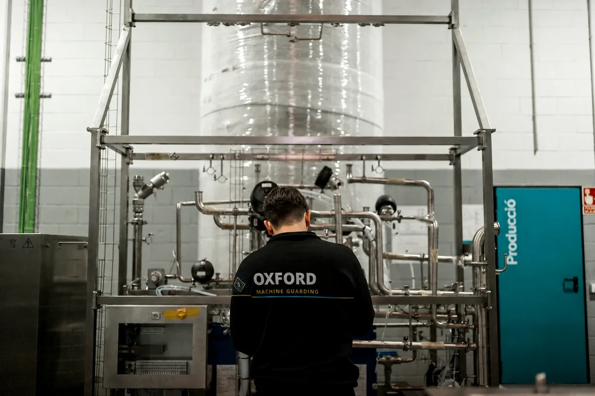 Person wearing an Oxford Machine Guarding jacket beside stainless steel process equipment.
